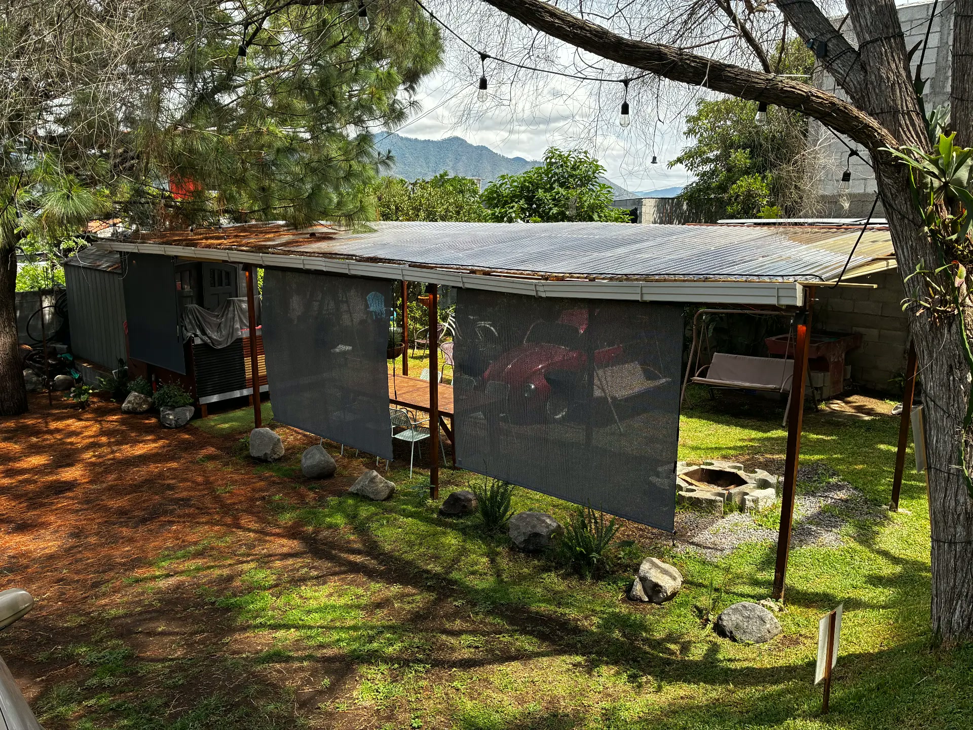 Vista del jardín de La Cumbre Coffee con pérgola techada, árboles, césped y vista al volcán de fondo